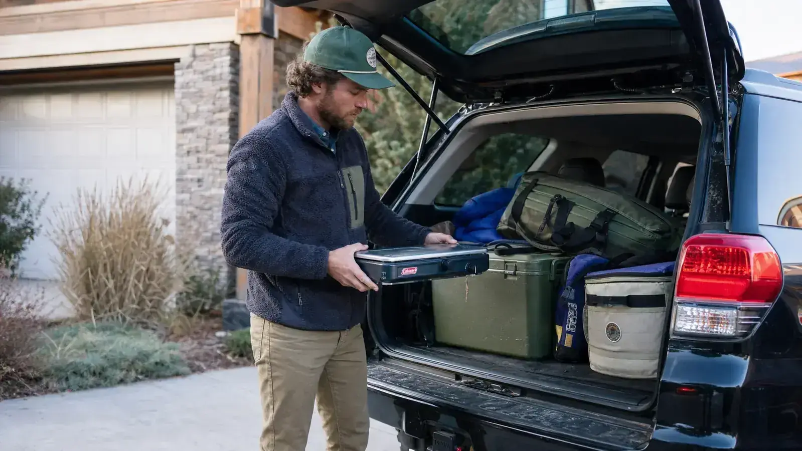 Coleman Triton stove folded and latched closed next to a camping backpack ready for transport in the back of a truck bed