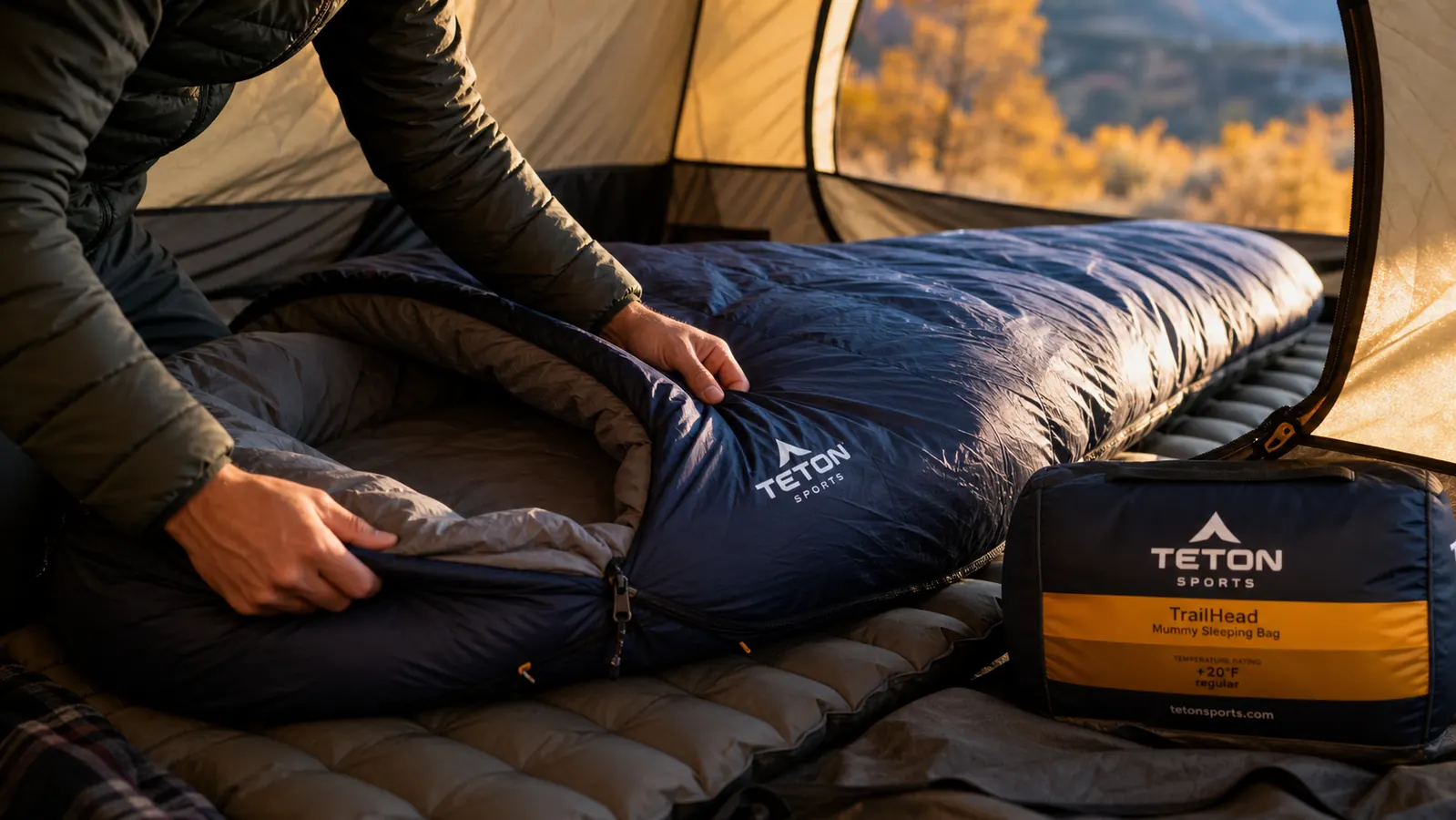 TETON Sports TrailHead mummy sleeping bag laid out on a sleeping pad inside a tent, with a wool base layer and beanie beside it